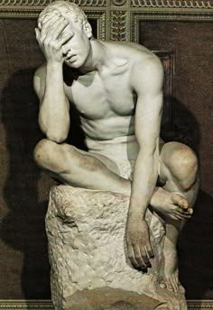 a man sitting on top of a rock next to a stone statue with his head in his hands