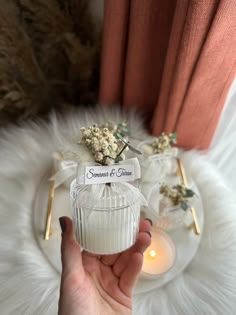 a person holding a candle in front of a window with some flowers on top of it