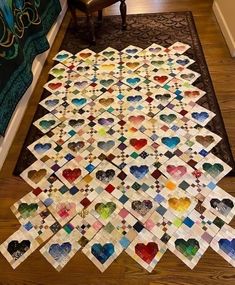 a large quilt is laying on the floor in front of a chair and rug that has hearts cut out of it