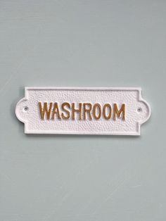 a white sign that says washroom on the side of a gray wall with gold lettering