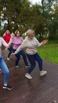 four women are dancing on a deck in the park