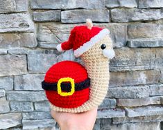 a hand holding up a crocheted santa clause hat with a snail on it