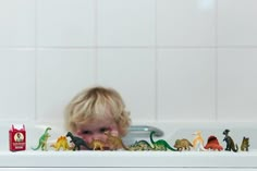 a little boy playing with toy dinosaurs in the bathtub