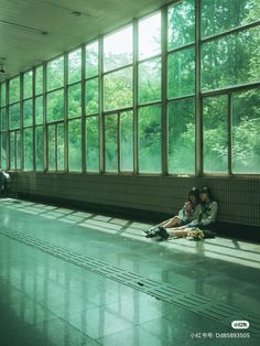 two people sitting on the floor in front of large windows