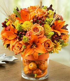 a vase filled with lots of orange flowers and pumpkins on top of a table