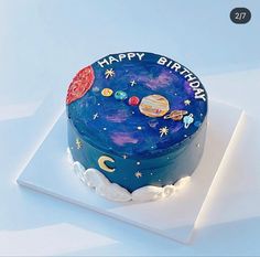 a blue birthday cake with planets and stars on it sitting on a white tablecloth