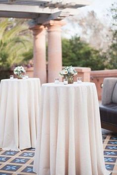 two tables covered with white tablecloths sitting on top of a tiled floor next to couches