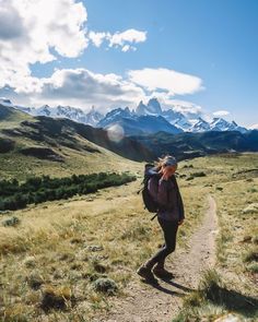 a woman with a backpack is walking on a trail in the mountains and has her back to the camera