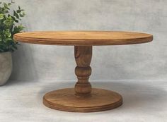 a round wooden table sitting next to a potted plant on top of a white surface