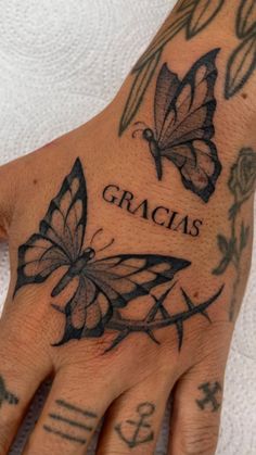 a person's hand with tattoos on it and two butterflies that say gracias