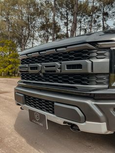 the front end of a silver truck parked on a dirt road with trees in the background