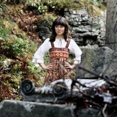 a woman standing in front of some rocks and trees with her hands on her hips