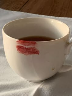 a cup filled with liquid on top of a white table cloth covered in red lipstick