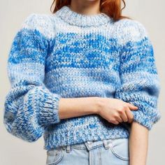 a woman with red hair is wearing a blue sweater and denim jeans, she has her hands on her hips