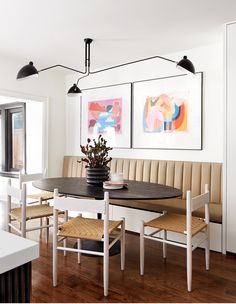 a dining room table and bench with two pictures on the wall above it, along with chairs