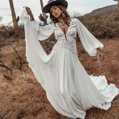 a woman in a long white dress and cowboy hat posing for the camera with her arms outstretched