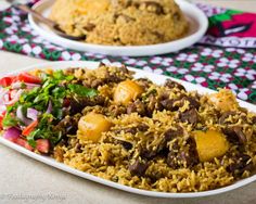 a white plate topped with rice covered in meat and veggies next to a bowl of salad