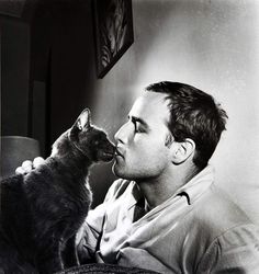 a man kissing a cat on the nose in a black and white photo with a lamp behind him