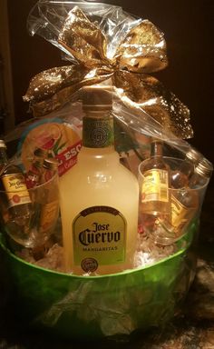 a bottle of alcohol sitting in a green basket with gold foil on the top and other items around it