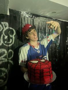 a young man holding up a cake with a spiderman design on it and pointing to the side