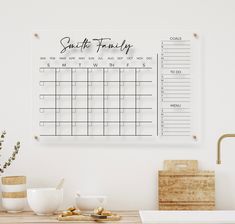 a calendar hangs on the wall above a wooden table with coffee cups and other items