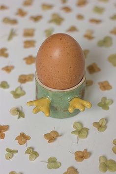 an egg sitting in a cup on top of a table covered with leaves and flowers