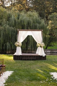 an outdoor wedding ceremony setup with white drapes and flowers on the altar, surrounded by willow trees