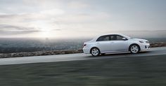 a white car driving down the road in front of a cityscape at sunset