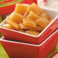 two red bowls filled with cubed fruit on top of a green tablecloth covered place mat