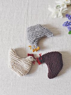 three crocheted chickens on a table next to some flowers and bluebells