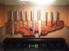 five knives are hanging on the wall above an oven and counter top with a clock