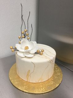 a white and gold decorated cake with flowers on the top is sitting on a table