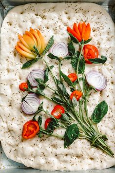 an uncooked pizza topped with vegetables and herbs