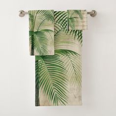 two towels hanging on a towel rack with palm leaves printed on them, one is green and the other is white