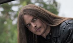 a man with long hair and leather jacket sitting in a car looking at the camera