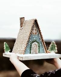 a person holding a tray with a gingerbread house on it and trees in the background