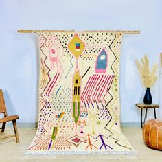 a colorful rug is hanging on the wall next to two wooden chairs and a vase