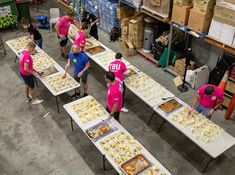 people in pink shirts standing around tables with food on them