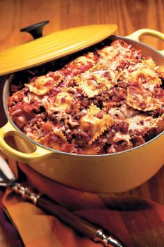 a casserole dish with meat and cheese in it on a wooden table next to utensils