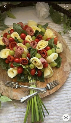 a wooden plate topped with lots of food on top of a table next to utensils