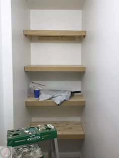 some shelves in the corner of a room with plastic bags on them and a green trash can next to it