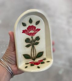 a hand holding a white and red vase with flowers on it