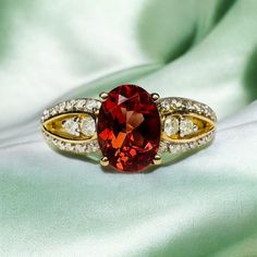 a fancy ring with a red stone surrounded by white and yellow diamonds on a green cloth