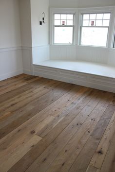 an empty room with wooden floors and two windows in the wall, along with a window seat