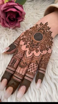 a woman's hand with henna tattoos on it and flowers in the background