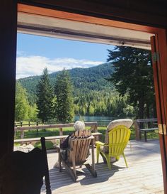 an elderly woman sitting at a table on a deck with mountains in the back ground