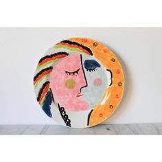 a colorful plate with a woman's face painted on the front and side, against a white wall