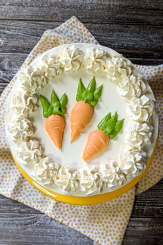 a cake decorated with three carrots on top of a wooden table next to a napkin