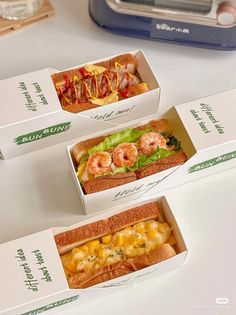 three boxes filled with different types of food on top of a white table next to a toasted sandwich