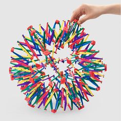 a hand is holding a colorful object in the shape of a circle with colored sticks sticking out of it